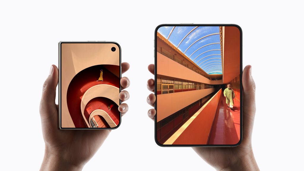Zwei Hände halten jeweils ein modernes Smartphone. Das linke Smartphone zeigt ein Bild einer spiralförmigen Treppe mit einer Person darauf. Das rechte Smartphone zeigt eine moderne architektonische Ansicht mit einem Mann in einem langen Gewand unter einem Gewölbedach.